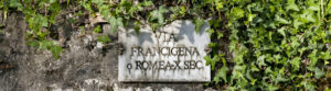 Insegna marmorea della Via Francigena affissa su un muro con edera